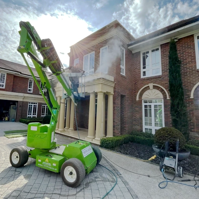 Pressure washing large surrey mansion on a cheery picker in driveway.