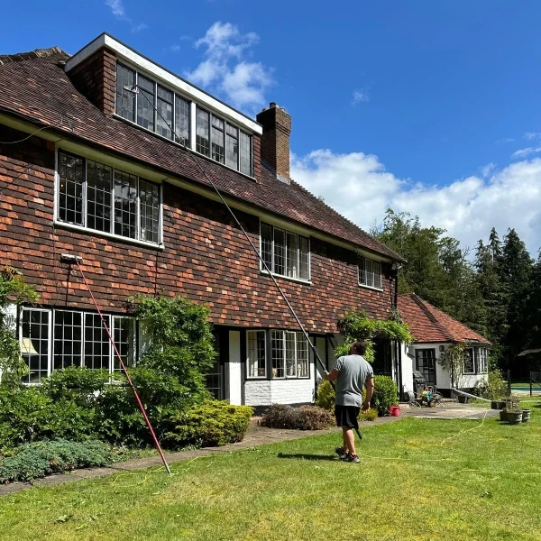 Man cleaning windows o large surrey house with pole fed system.